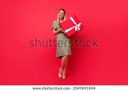 Photo of funny charming young woman dressed green clothes holding big present box smiling isolated red color background