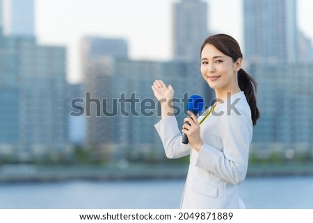 Young asian announcer reporting in front of the city. Royalty-Free Stock Photo #2049871889