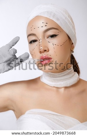 ffashionable portrait of a young beautiful Asian woman with markings on her face.on an isolated background with a syringe in his hands. the syringe contains injections of drugs for cosmetology.