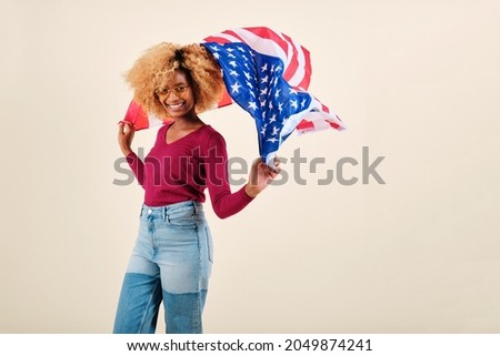 Smiling young afro woman waving a US flag while standing on an isolated background.