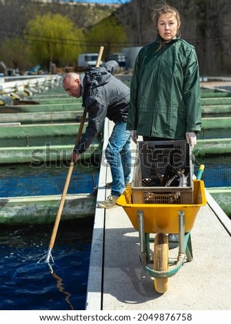 Male and female fish farm workers catching sturgeon at pools