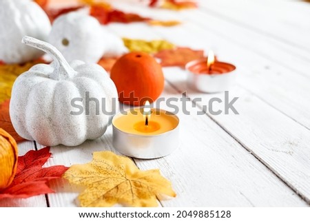 Autumn decoration with white decorative pumpkins, candles and colorful maple leaves on white wooden background. Autumn vibes. Thanksgiving decor. Space for text. Selective focus.