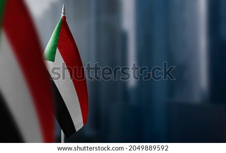 Small flags of Sudan on a blurry background of the city Royalty-Free Stock Photo #2049889592