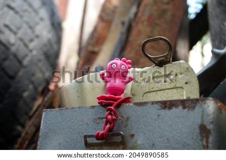 A small pink plastic alien toy for children and tin can. Funny monster close-up photo against the background of tires and iron sheets.