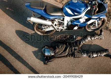 Motorcyclist in leather protective suit and a black helmet lies on the asphalt near a sports motorcycle. Biker in black on the road. View from above