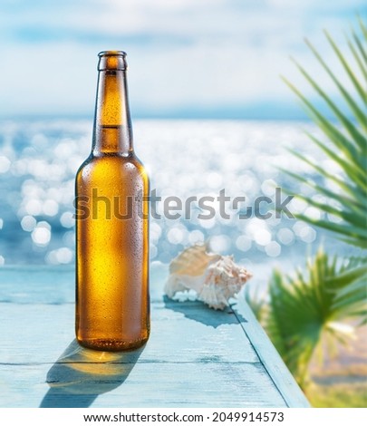 Opened bottle of beer with condensation on the wooden table. Blurred sparkling sea at the background. Summer vibes. Royalty-Free Stock Photo #2049914573
