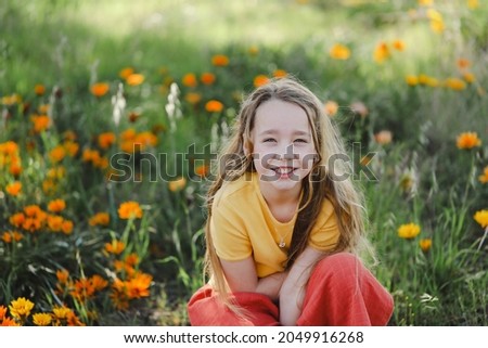 Portrait of pretty girl sitting in field with vibrant orange and yellow wildflowers