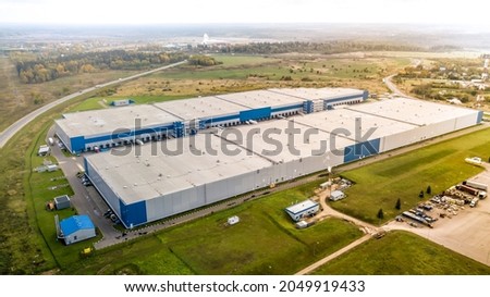 Aerial shot of industrial warehouse. Loading hub and many trucks with cargo trailers. Aerial view of goods warehouse. Modern Distribution Center from outside. Aerial view of warehouse with trucks. 