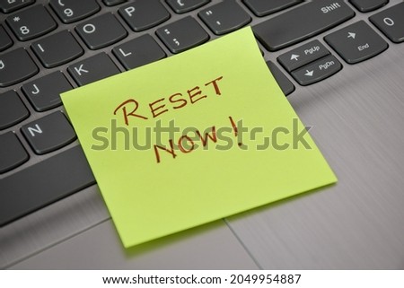 RESET NOW! handwritten words on sticky note laid on laptop keyboard. Concept of resetting password for security protection. 