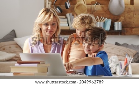 Happy family at home, mother with son and daughter have fun using computer, parent with children browsing internet on laptop, child student shows something pointing at the monitor
