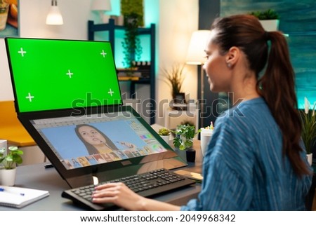 Woman photographer doing retouching work at studio with green screen, display chroma key for mockup template and isolated background. Colour professional editing photo for project