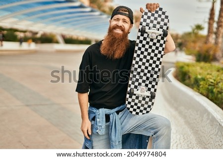 Young irish skater man smiling happy holding skate at the city.