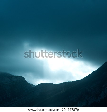 Square photo of dramatic rays of light pushing up through clouds