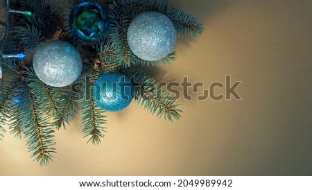 blue and gray shiny Christmas balls are lying on the branch of a blue Christmas tree with a garland on a beige background. top view