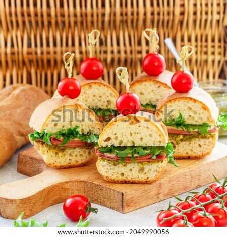 Baguette sandwiches with pesto sauce, sausage or ham, cheese, lettuce and cherry tomatoes. Picnic food. Selective focus, copy space, square picture