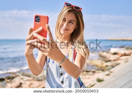 Young blonde girl smiling happy making selfie by the smartphone at the beach.