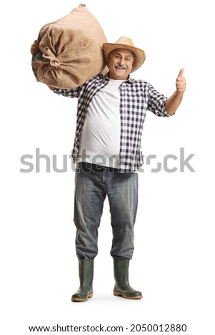 Full length portrait of a mature farmer carrying a big burlap sack on his shoulder and gesturing thumbs up isolated on white background