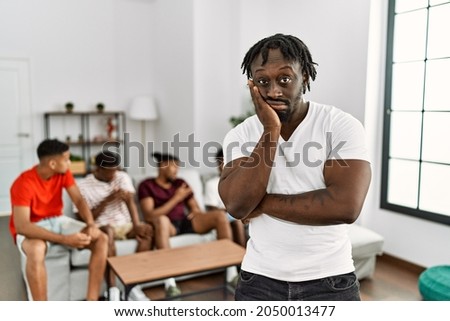 Young african man with friends at the living room thinking looking tired and bored with depression problems with crossed arms. 