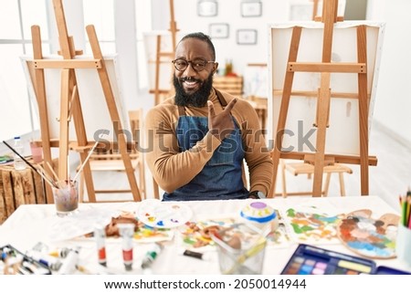 African american artist man at art studio cheerful with a smile of face pointing with hand and finger up to the side with happy and natural expression on face 