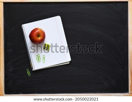 School supplies on a black chalkboard, copybook and an apple. Back to school.