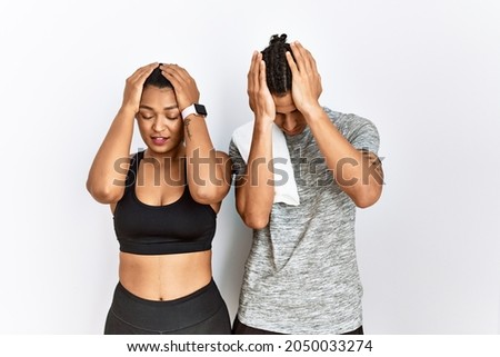 Young latin couple wearing sportswear standing over isolated background suffering from headache desperate and stressed because pain and migraine. hands on head. 