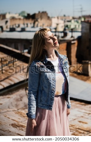 happy young woman stands on the rusty rooftops of the city and enjoys the sunbeams. tourist on the St. Petersburg rooftops. tourist trend. visiting card of the city.