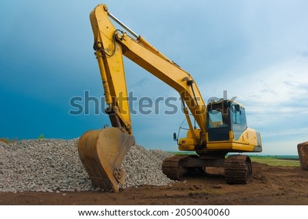 A modern yellow excavator against the sky is located at a construction site.