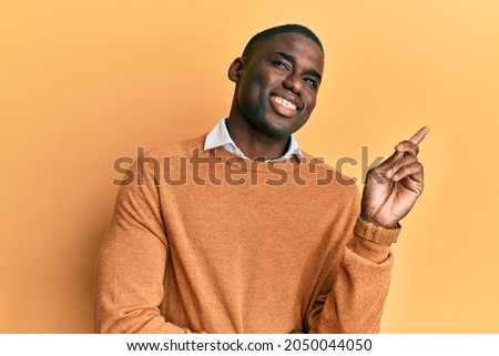 Young african american man wearing casual clothes with a big smile on face, pointing with hand and finger to the side looking at the camera. 