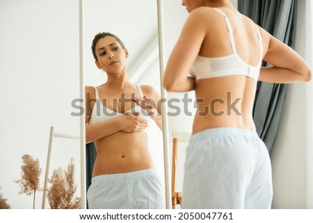 Young woman doing breast self-examination while looking herself in a mirror at home. Royalty-Free Stock Photo #2050047761
