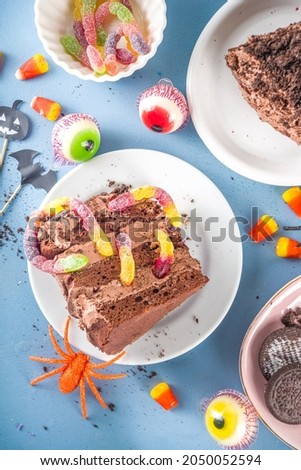 Funny creepy holiday cake for Halloween kids party, Creative dessert idea, chocolate cake piece with marmalade worms, traditional Halloween sweets and candy, copy space