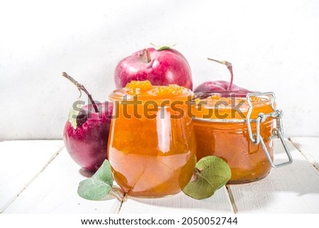 Homemade golden colored apple jam, with farm red apples and leaves on white wooden background copy space