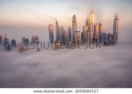 Skyline of Dubai Marina covered in thick fog. Sunrise picture. Buildings glowing up. 