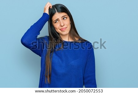 Young hispanic woman wearing casual clothes confuse and wonder about question. uncertain with doubt, thinking with hand on head. pensive concept.  Royalty-Free Stock Photo #2050072553