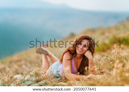 A young beautiful woman is lying on the grass on the mountainside at sunset. The concept of enjoying nature