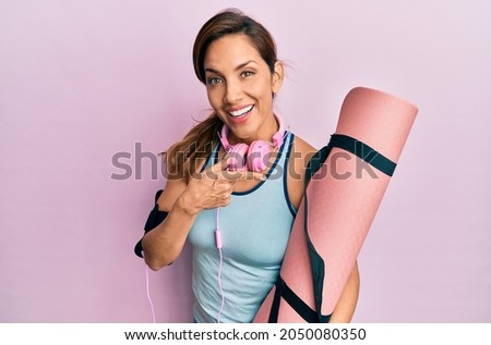 Young latin woman holding yoga mat smiling happy pointing with hand and finger 