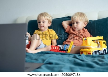 cute little caucasian kids boys twins using laptop in bed at home. Kids using technology.