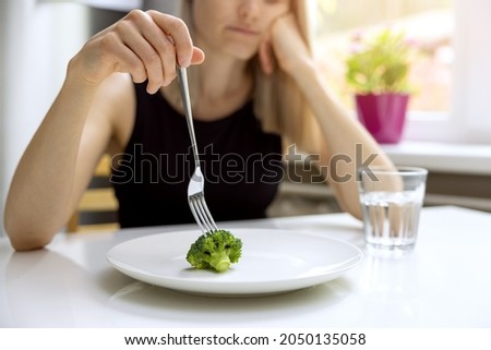 dieting problems, eating disorder - unhappy woman looking at small broccoli portion on the plate Royalty-Free Stock Photo #2050135058