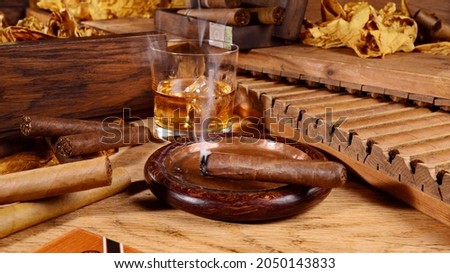 Cigars with Whisky and Tobacco Leaves on wooden Background. Smoking Cigar in an Ashtray. Royalty-Free Stock Photo #2050143833