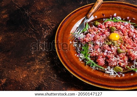 Beef steak tartare with raw egg yolk, pickled capers and Parmesan cheese. Dark background. Top view. Copy space