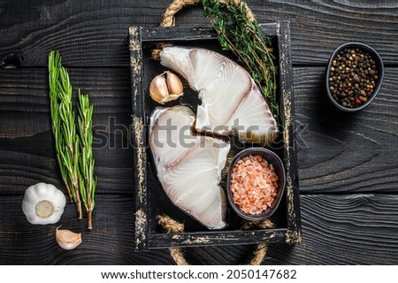Shark raw fish steaks in a wooden tray with herbs. Black wooden background. Top view. Copy space.
