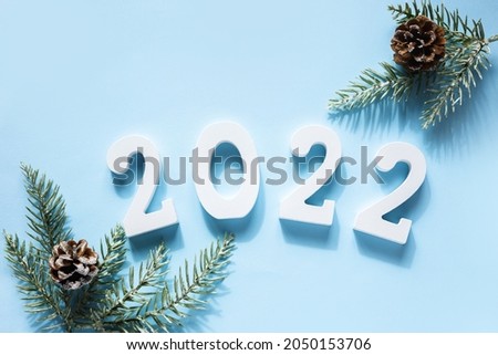 Happy New Year. White wooden numbers 2022, green branches fir tree, cone on blue background . Greeting card. Top view, flat lay.