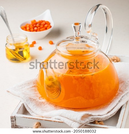 Vitamin hot sea buckthorn tea in a small glass teapot with fresh raw sea buckthorn berries and honey. Seasonal healthy drink. Selective focus, square picture