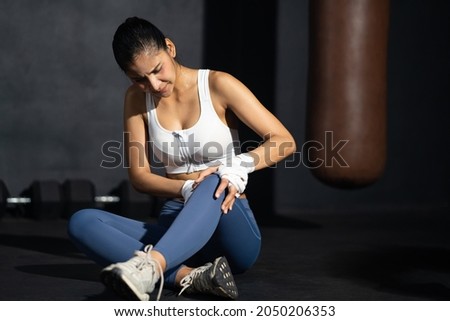 Young adult Asian women feeling painful from knee muscle injury after workout with weight lifting, cross training at fitness gym. Muscle injured from workout or exercise, weight training. Royalty-Free Stock Photo #2050206353
