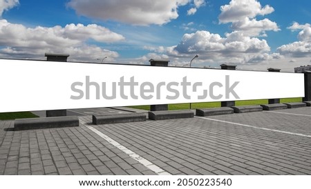 Long white empty vinyl banner fixed on concrete fence at parking lot on city street under blue sky with huge clouds