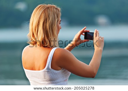Back view of young pretty woman taking photos with mobile phone.