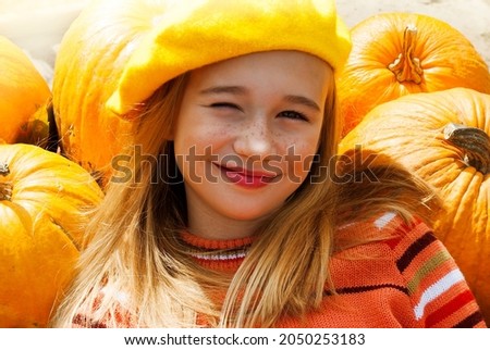 Funny, beautiful teenage girl on the background of the pumpkin. Cute baby with freckles in a bright yellow beret. Holidays autumn concept: Halloween or Thanksgiving. 