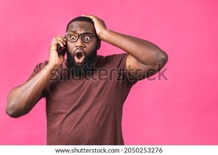 Closeup portrait of handsome african american black man, shocked, surprised, wide open mouth, using mobile phone, isolated on pink background. Negative human emotions.