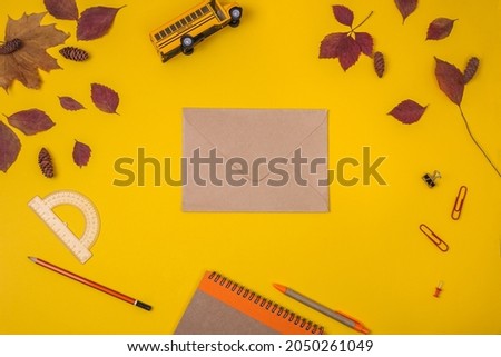 Mockup. Kraft organic paper envelope. Recycled paper notebook, school bus, pen, pensil and protractor on a yellow backgroun. Autumn. Time to go to school. Autumn foliage.