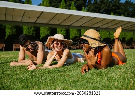 Cheerful friends rest on the grass near the pool