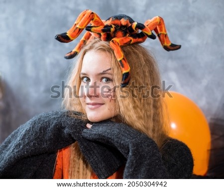 Teenage girl among decor for Halloween holiday, huge spider on her head. Close up photo, orange blakc colors